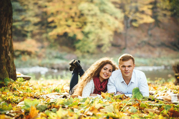 Happy young couple lying among autumn leaves at the park.