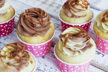 Vanilla cupcakes with a cap of cream on white wooden table