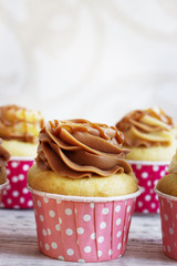 Vanilla cupcakes with a cap of cream on white wooden table