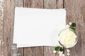 white cosmetic beeswax pellets in bowl on blank recipe paper.
