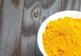 Turmeric powder in white cup on wooden floor.