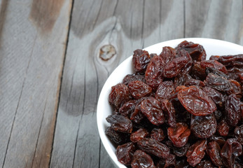 Dried grapes in white cup on wooden floor.