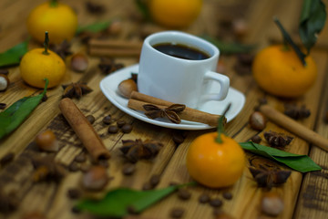Small white cup of coffee, cinnamon sticks, cocoa beans, star anise, hazelnuts and mandarins on wooden background