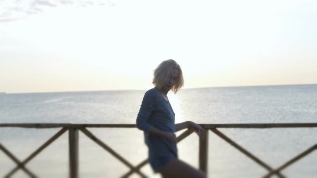 Blond girl in denim shorts dancing happy near the beach at beautuful sunrise