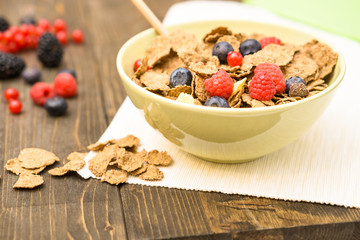 Cereal and berries breakfast bowl on old wood table cropped image - Healthy meal concept with wheat bran flakes and mixed red fruits