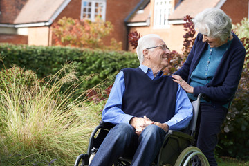 Fototapeta na wymiar Senior Man Being Pushed In Wheelchair By Wife