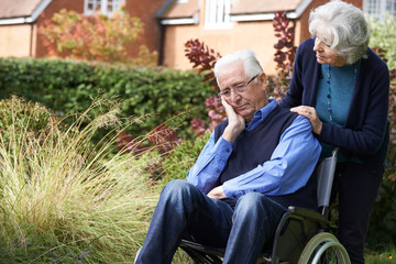 Fototapeta na wymiar Depressed Depressed Senior Man In Wheelchair Being Pushed By Wif