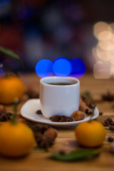 Small white cup of coffee, cinnamon sticks, cocoa beans, star anise, hazelnuts and mandarins on wooden background