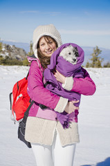 beautiful tourist woman hugging her cute little dog wrapped in blanket in the winter mountain