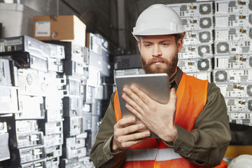 Worker in computer recycling plant using digital tablet