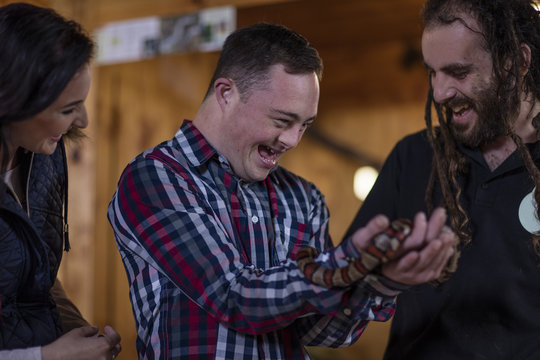 Animal attendant handing over coral snake to young man with down syndrome