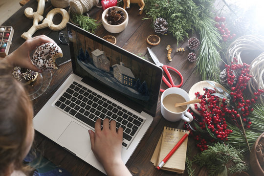 Woman eating bagel while working with laptop, partial view