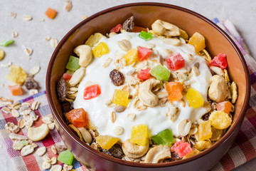 Healthy breakfast with yogurt, muesli and candied fruit in ceramic bowl on stone background