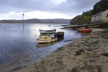 Boats anchored in lapping rippled water, row boats on a river with sand feathered near the shore moving, relaxed shot.