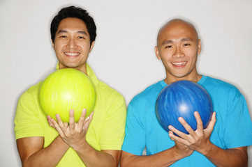 Two men standing side by side, carrying bowling balls, smiling at camera