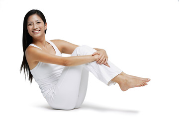 Woman sitting on floor, hugging knees, and lifting legs of floor, smiling