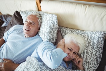 Man snoring and woman covering her ears while sleeping on bed