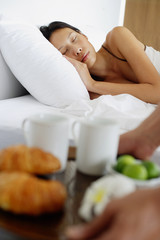 Obraz na płótnie Canvas Woman sleeping in bed, man setting down breakfast tray