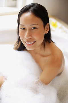 Woman in bathtub, covered with soap suds, smiling at camera