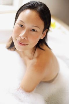Woman in bathtub, covered with soap suds, smiling