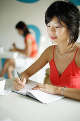 Young woman in cafe, writing in notebook