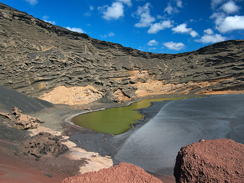Fototapeta The poisonous green volcanic lake in the crater caldera. Black hardened lava and the erosion of the slopes on the background of deep blue sky with white clouds. El Golfo, Canary Islands, Spain