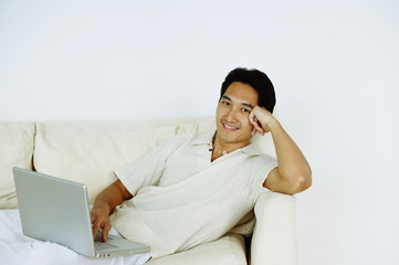 Man lying on sofa, using laptop, hand on head