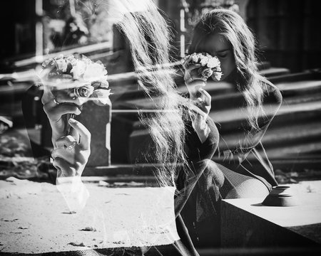 Monochrome double exposure of sad widow holding flowers near grave