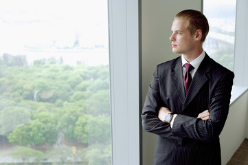 Fototapeta premium Businessman standing next to window in conference room, arms crossed