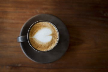 Hot latte art with  black glass on wooden table