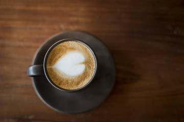 Hot latte art with  black glass on wooden table