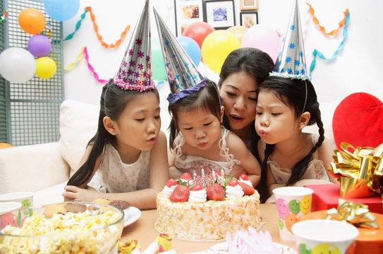 Mother with three girls celebrating a birthday, blowing candles on cake