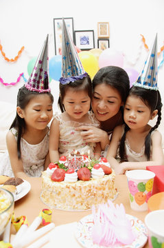 Mother with three daughters celebrating a birthday, looking at cake