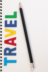 Travel word write on wooden alphabet and notebook on white background. The colorful word wooden travel with pencil on notebook background. Travel word concept. 