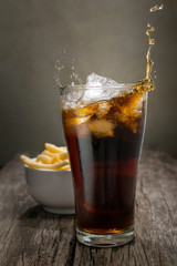 Cola glass with falling ice cubes on wood table.