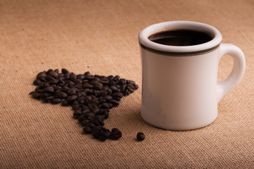 Coffee cup with beans in shape of South America on burlap, with a light vignette