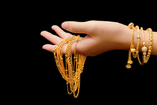 woman's hand with many different gold jewelry on black backgroun