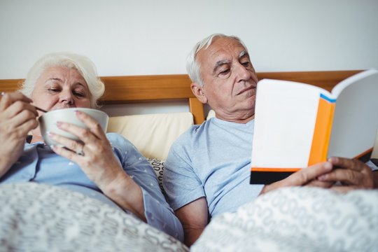 Senior man reading novel and woman having breakfast