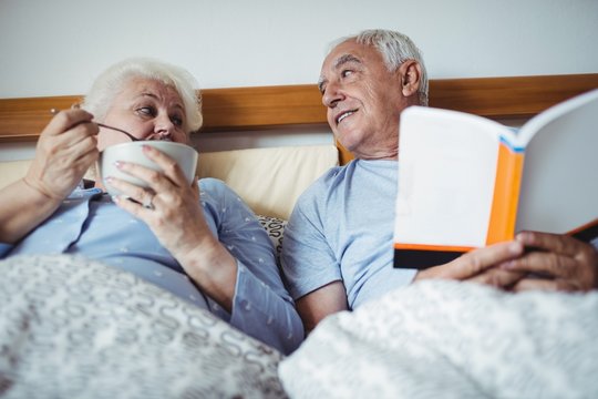 Senior man reading novel and woman having breakfast