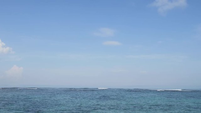 Airplane landing on island Bali airport under blue sea with waves on the horizon. Cinematic shot of overhead flying aircraft with shadow on beautiful ocean on cloudy sky background. Focal length 28mm