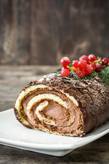 Fototapeta na wymiar Chocolate yule log cake with red currant on wooden background