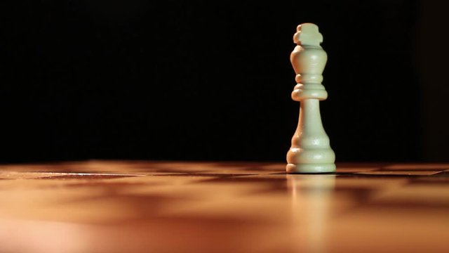 Low angle shot of the king chess peaces standing on a chess board and the white king hits and overthrows the black king and takes his place....