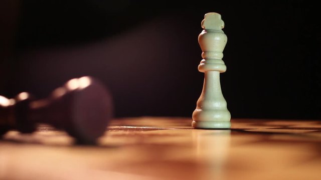 Low angle shot of the king chess peaces standing on a chess board and the white king hits and overthrows the black king and takes his place