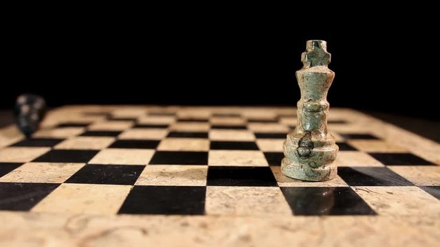 Two kings standing on a chess board, isolated on black background, the white king overthrows the black king...