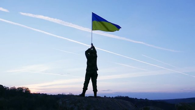 Soldier hold Ukrainian Flag Against Sunrise Sky. Slow Motion 