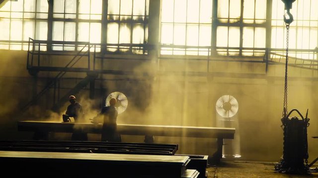 workers at the plant or factory processed metal. Purify by rust, sanded and polished by hand. Flying dust. Large shop windows, the sun's rays. It looks like an old factory of the Great Depression