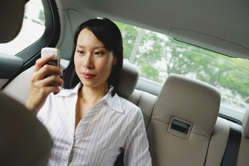 Fototapeta na wymiar Businesswoman in backseat of car using mobile phone, text messaging