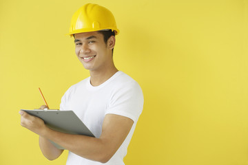 Man wearing hardhat, writing on clipboard, smiling at camera