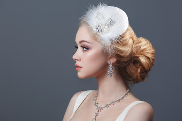 Beauty portrait of a cute blonde bride vintage hat with feathers isolated on a gray background.