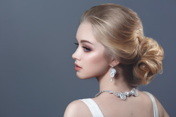 Beauty portrait of a cute blonde bride with beautiful hairstyle isolated on a gray background with back.